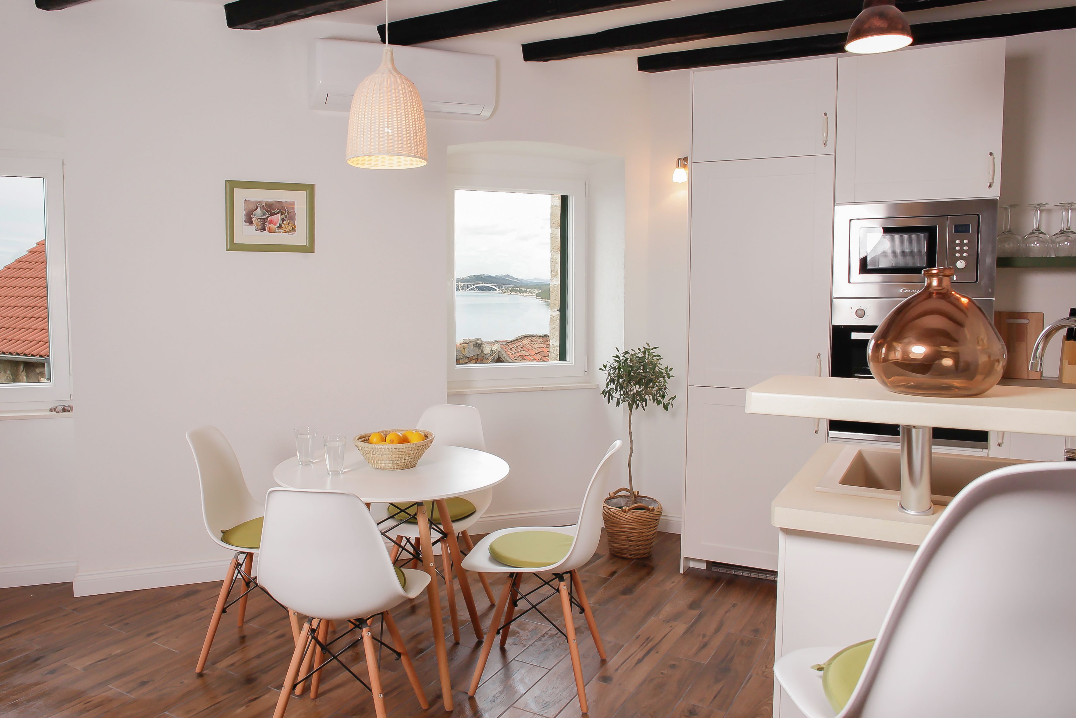 A modern kitchen with white cabinets, a stainless steel microwave, and a copper vase on the counter.