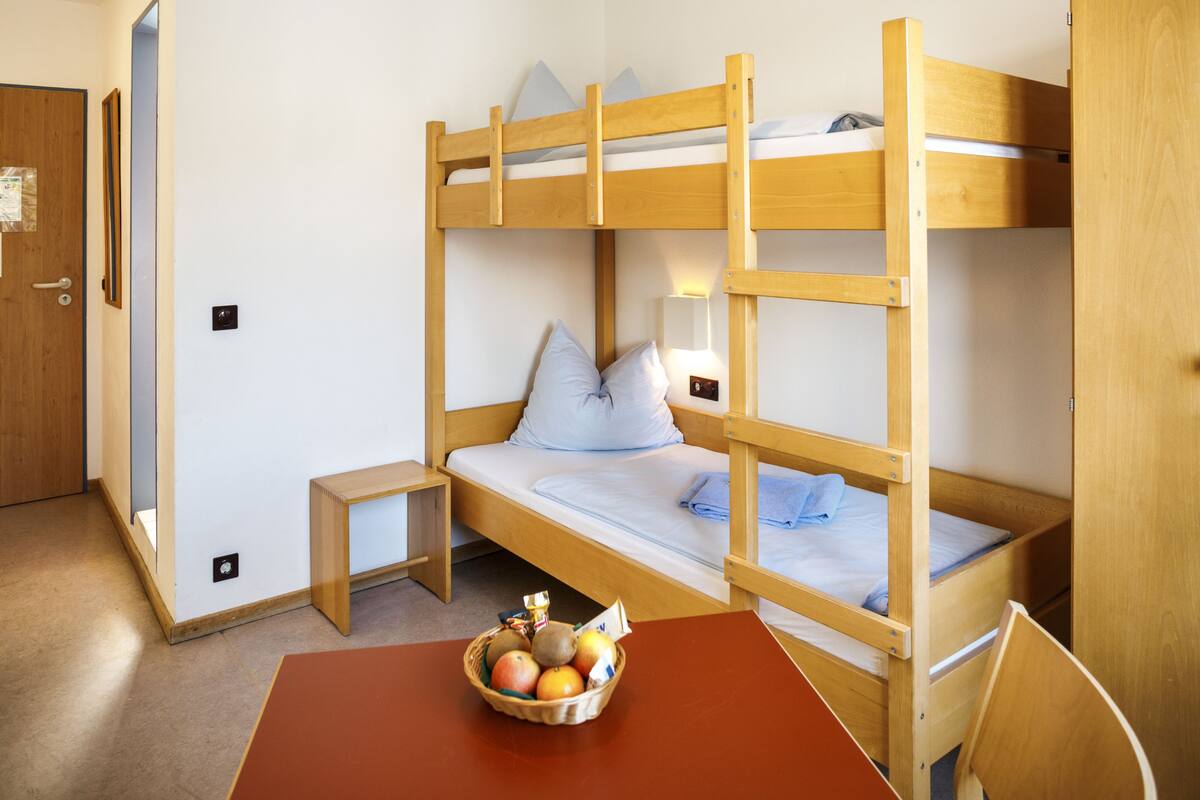 A bunk bed room with a small table and a fruit basket.