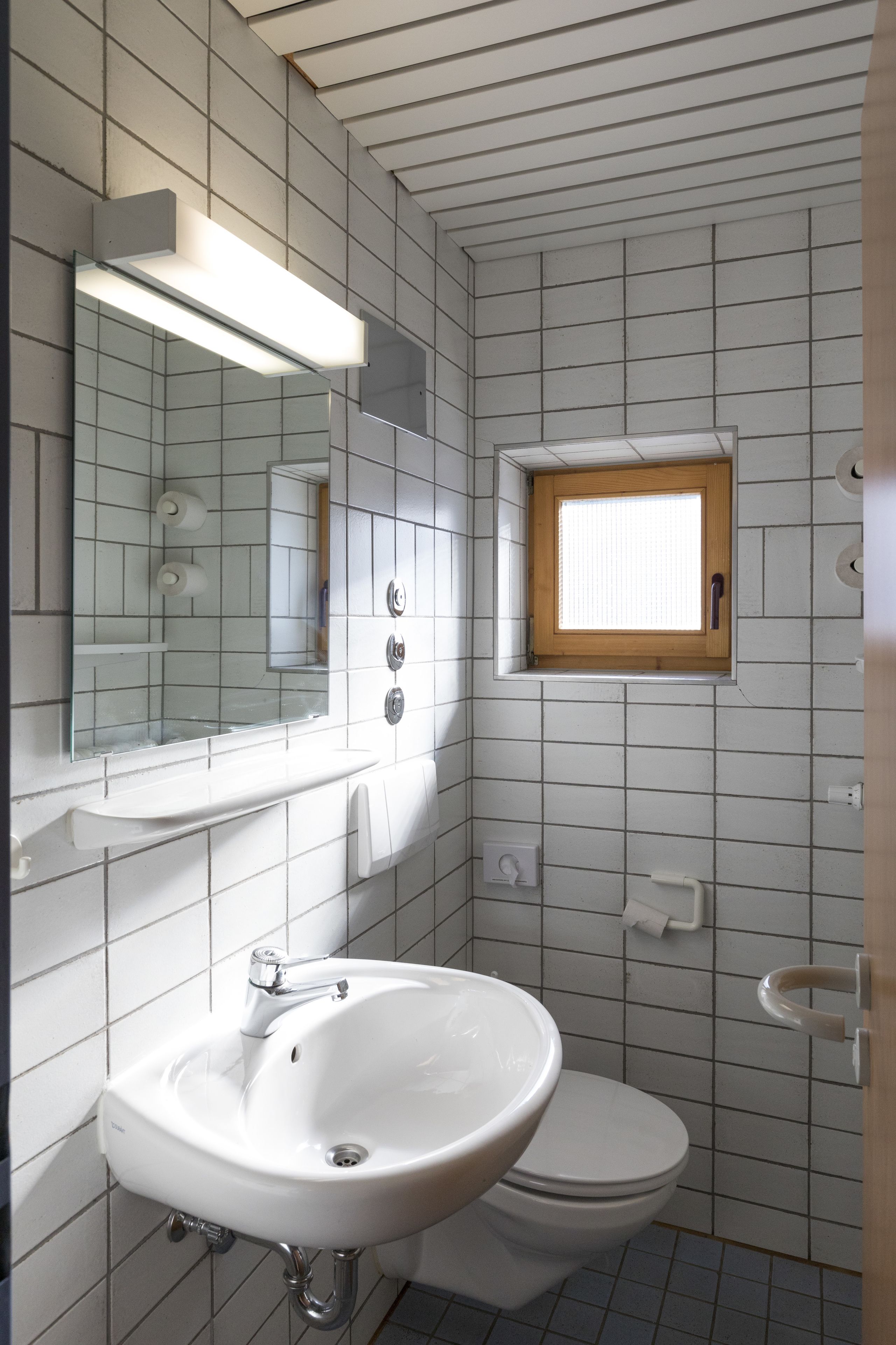 Une salle de bain avec un lavabo blanc, des toilettes, un miroir et une fenêtre.