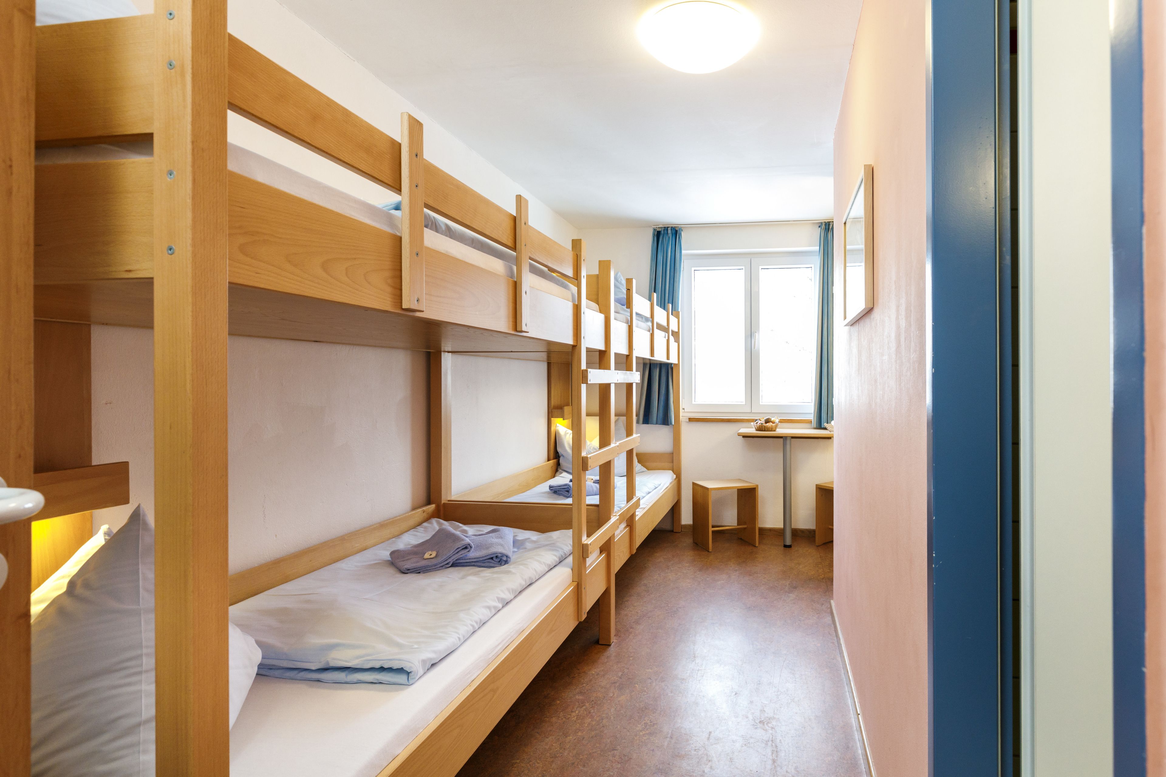 A bunk bed room with a small desk and window.