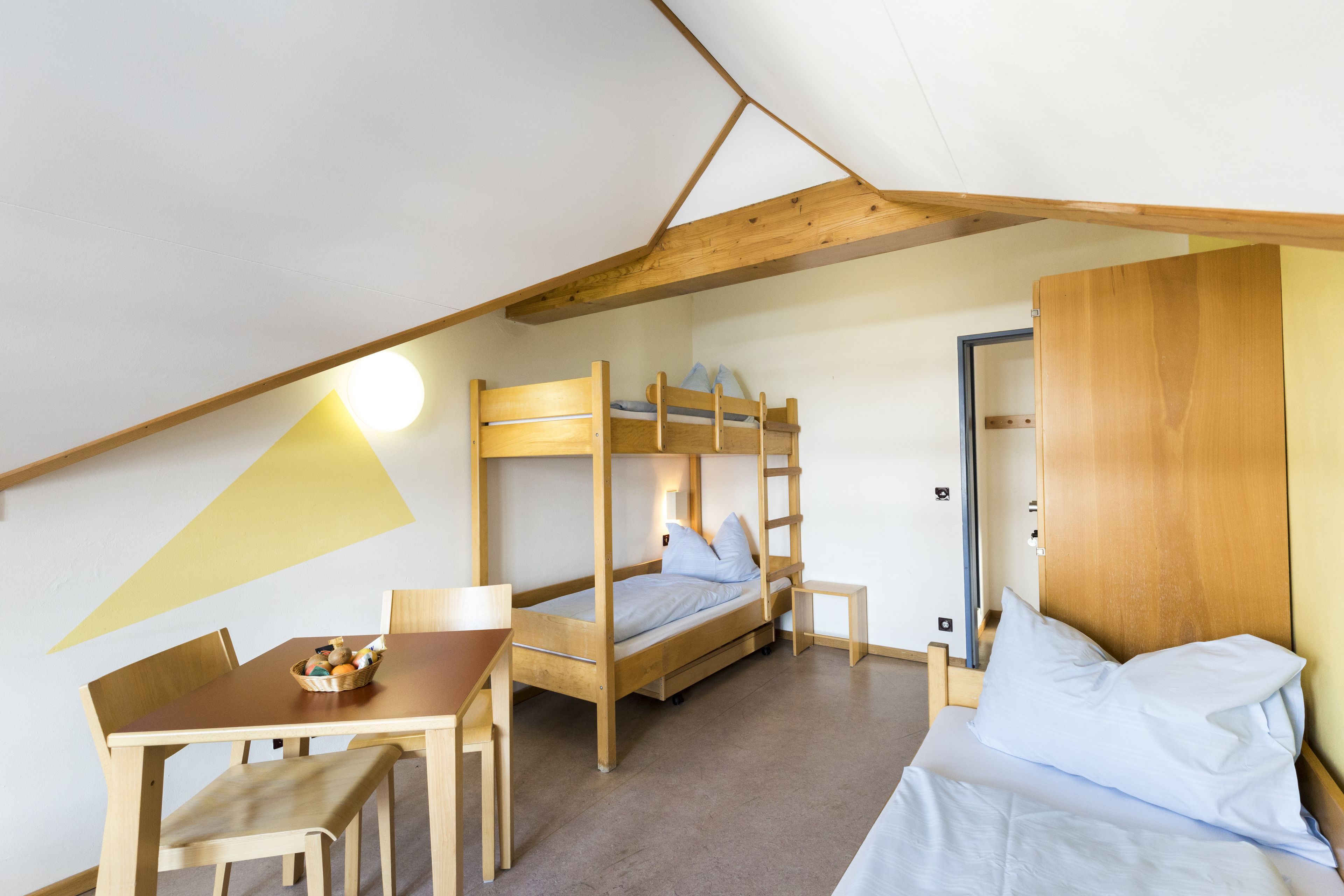 A dorm-style room with bunk beds, a wooden desk, and a small table.