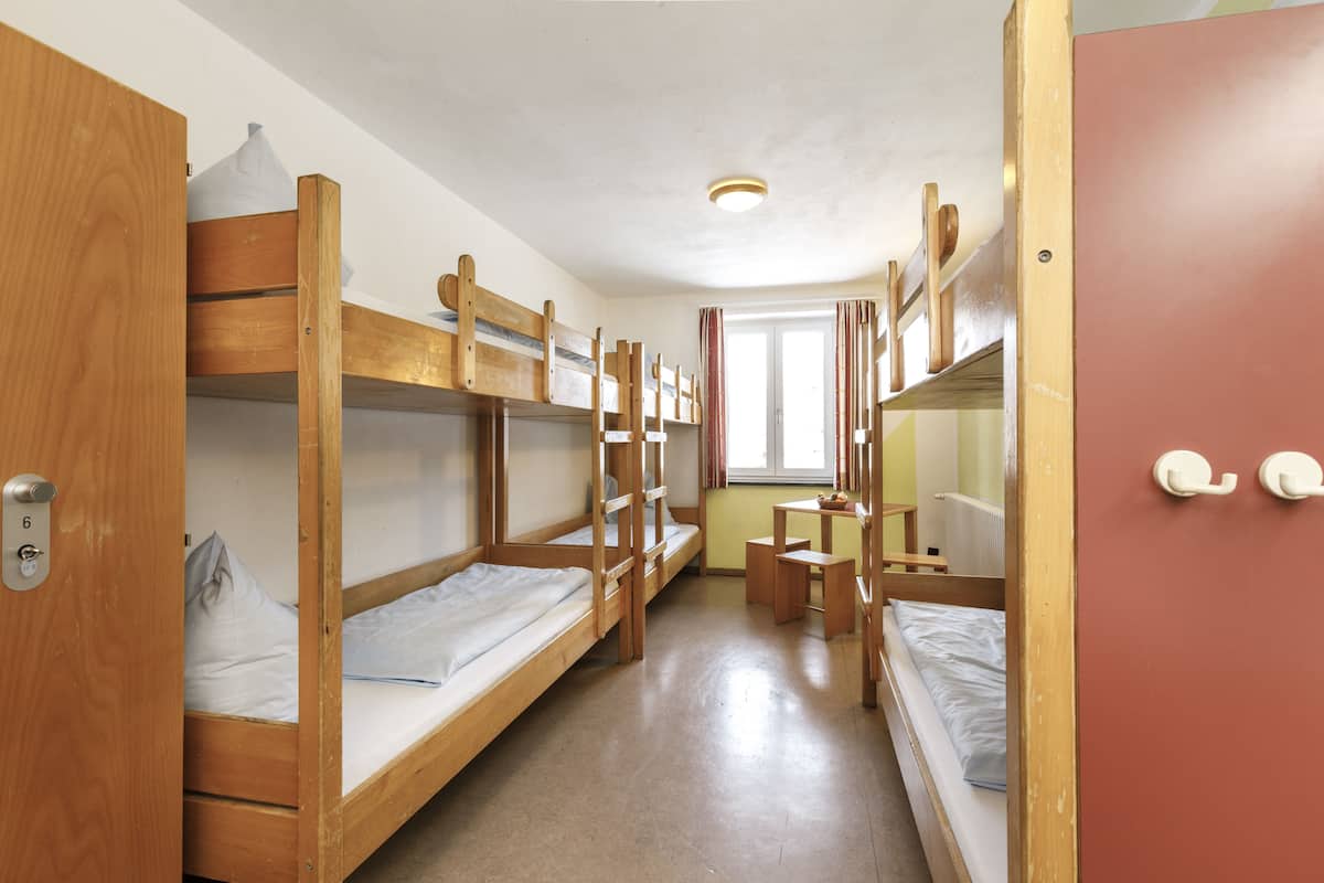 A dormitory room with bunk beds, a small table, and a window.