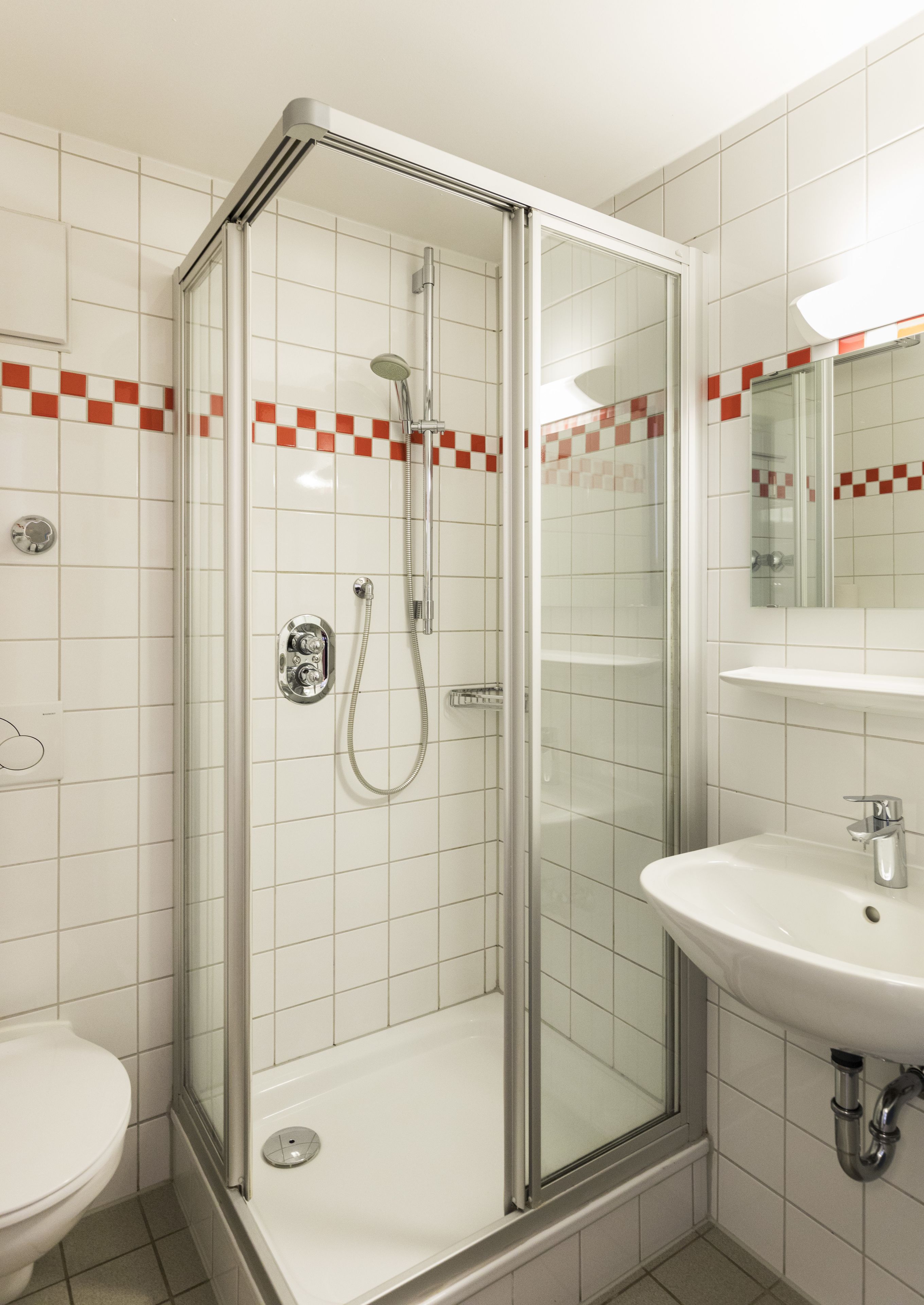 Un baño moderno con ducha de vidrio, lavamanos blanco y retrete.