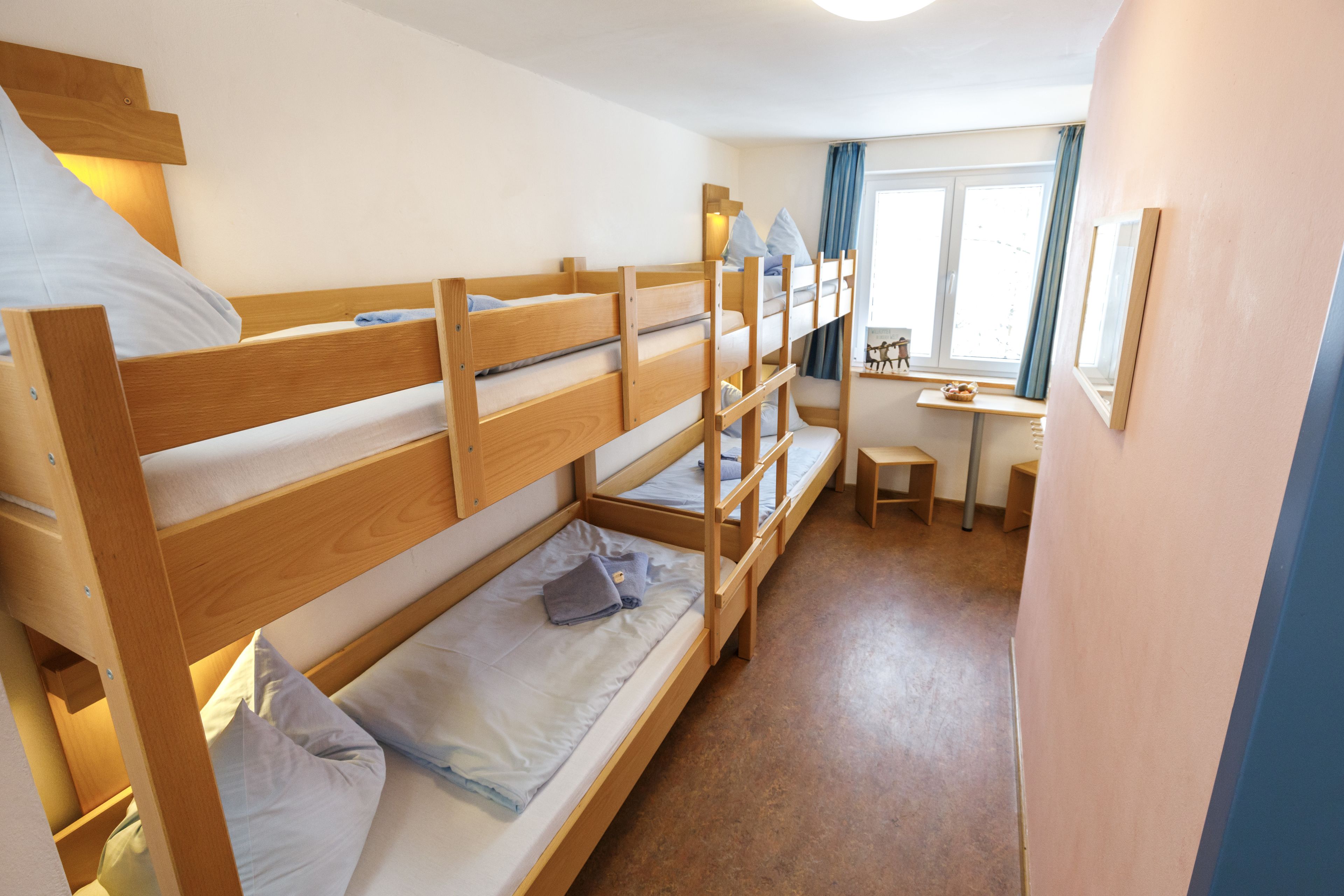Habitación con literas, escritorio, silla, ventana con cortinas y una mesita con lámpara.