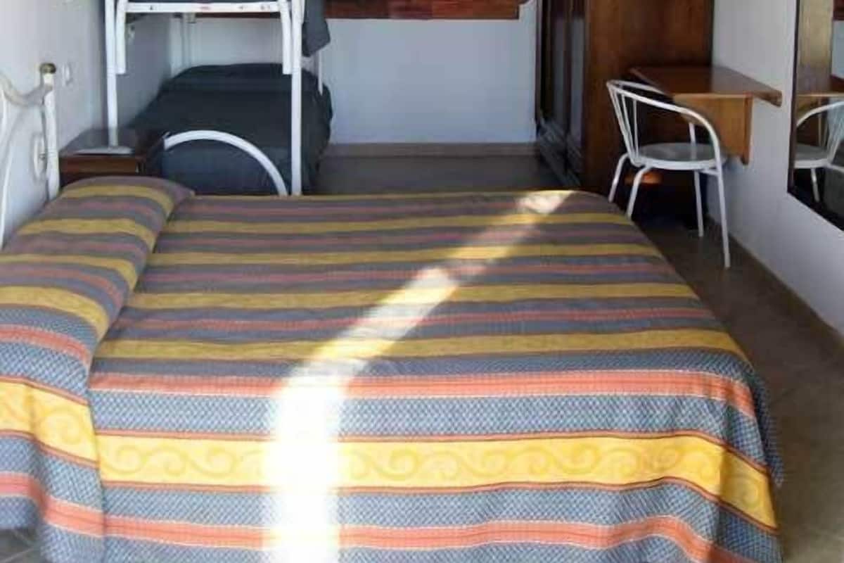 Un dormitorio con una cama, un escritorio, una silla, un televisor y una pared de ladrillo.