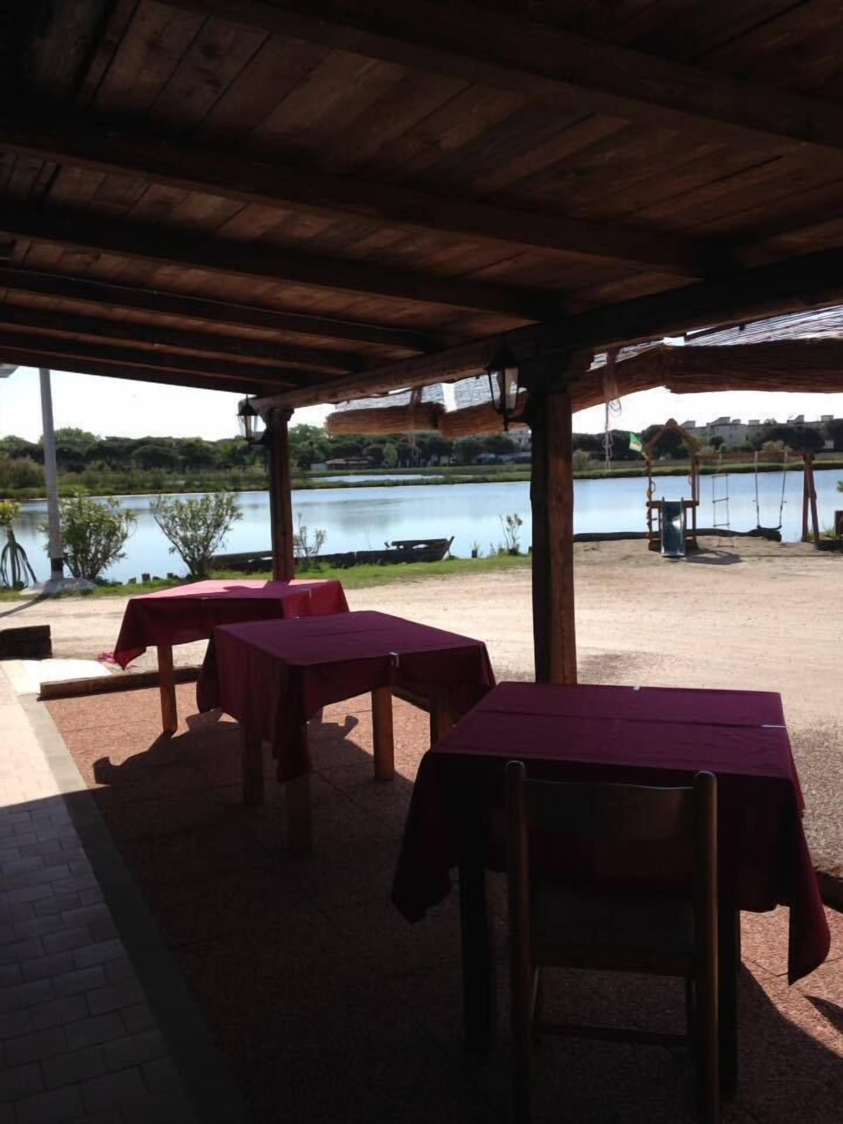Een terras met tafels en stoelen, met uitzicht op water en groen.
