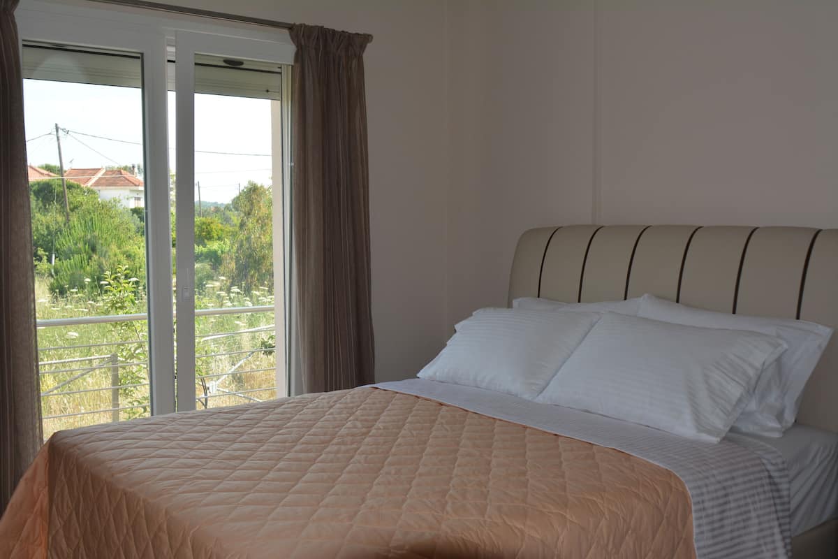 Un dormitorio con cama, cortinas y vistas al follaje exterior.
