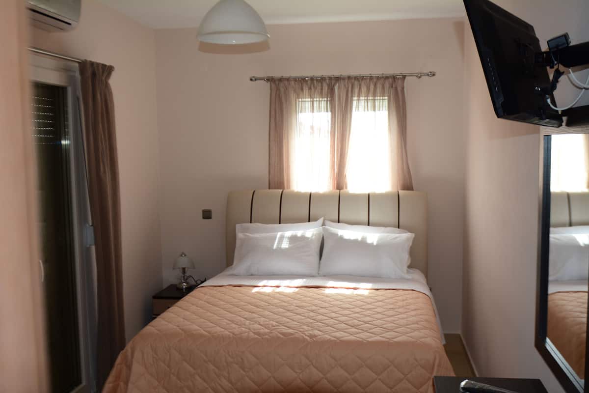 Habitación de hotel con cama, televisión montada en la pared y ventana con cortinas.