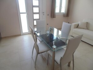 Un área de comedor con una mesa de vidrio y cuatro sillas, un sofá blanco y una puerta con ventanal.