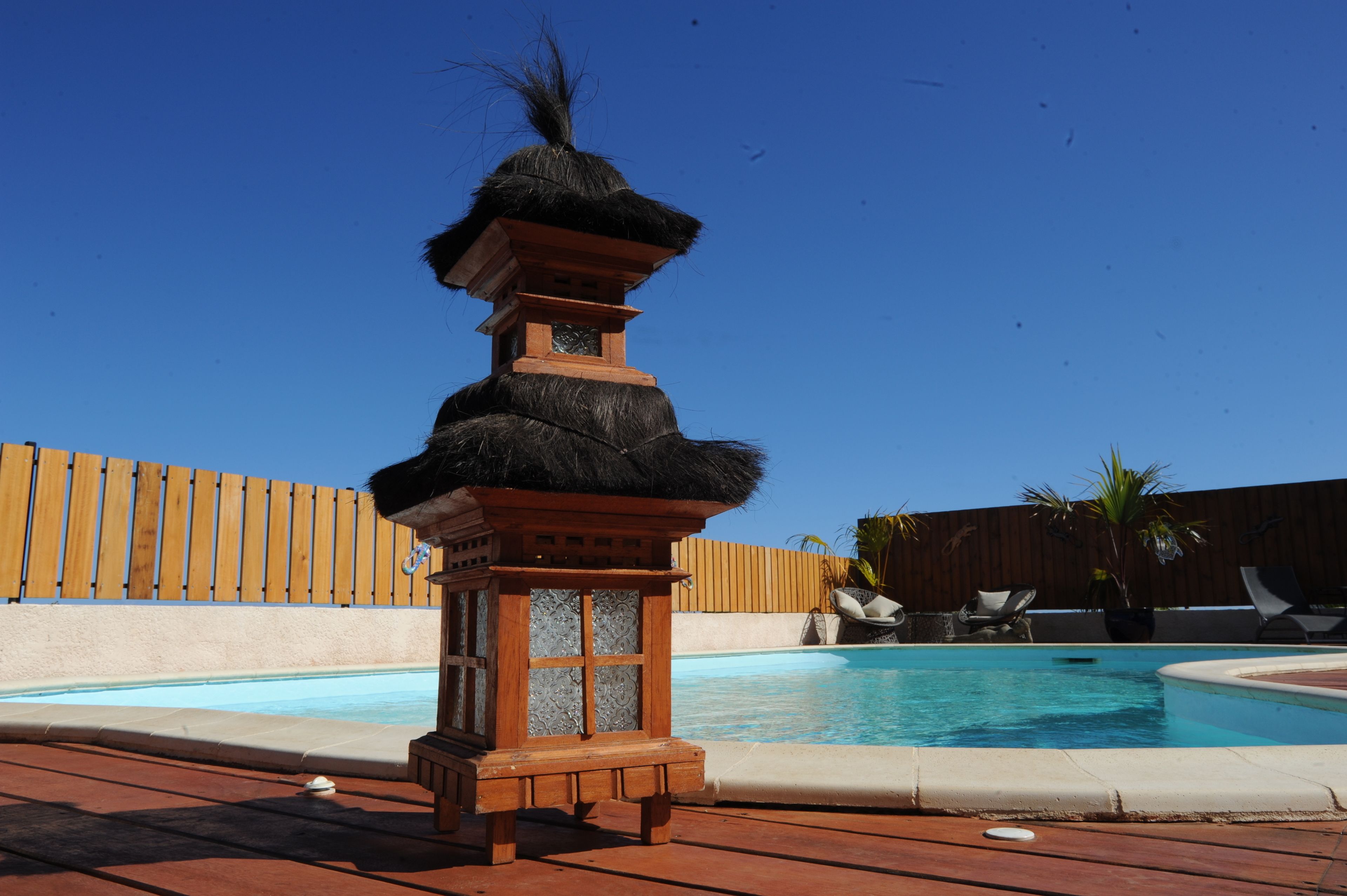 Een zwembadgedeelte met een decoratieve lantaarn, ligstoelen en een houten omheining.