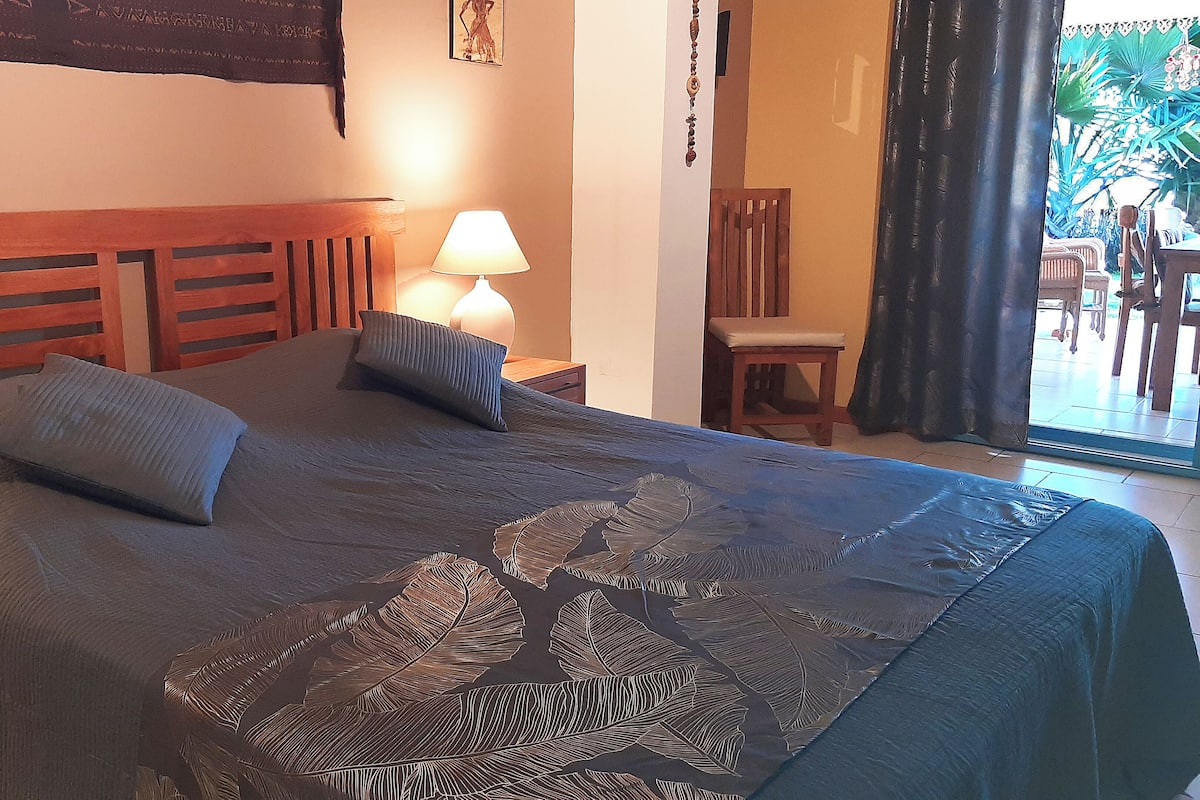 A hotel room with a bed, a nightstand, a lamp, a chair, and a view of the outside.