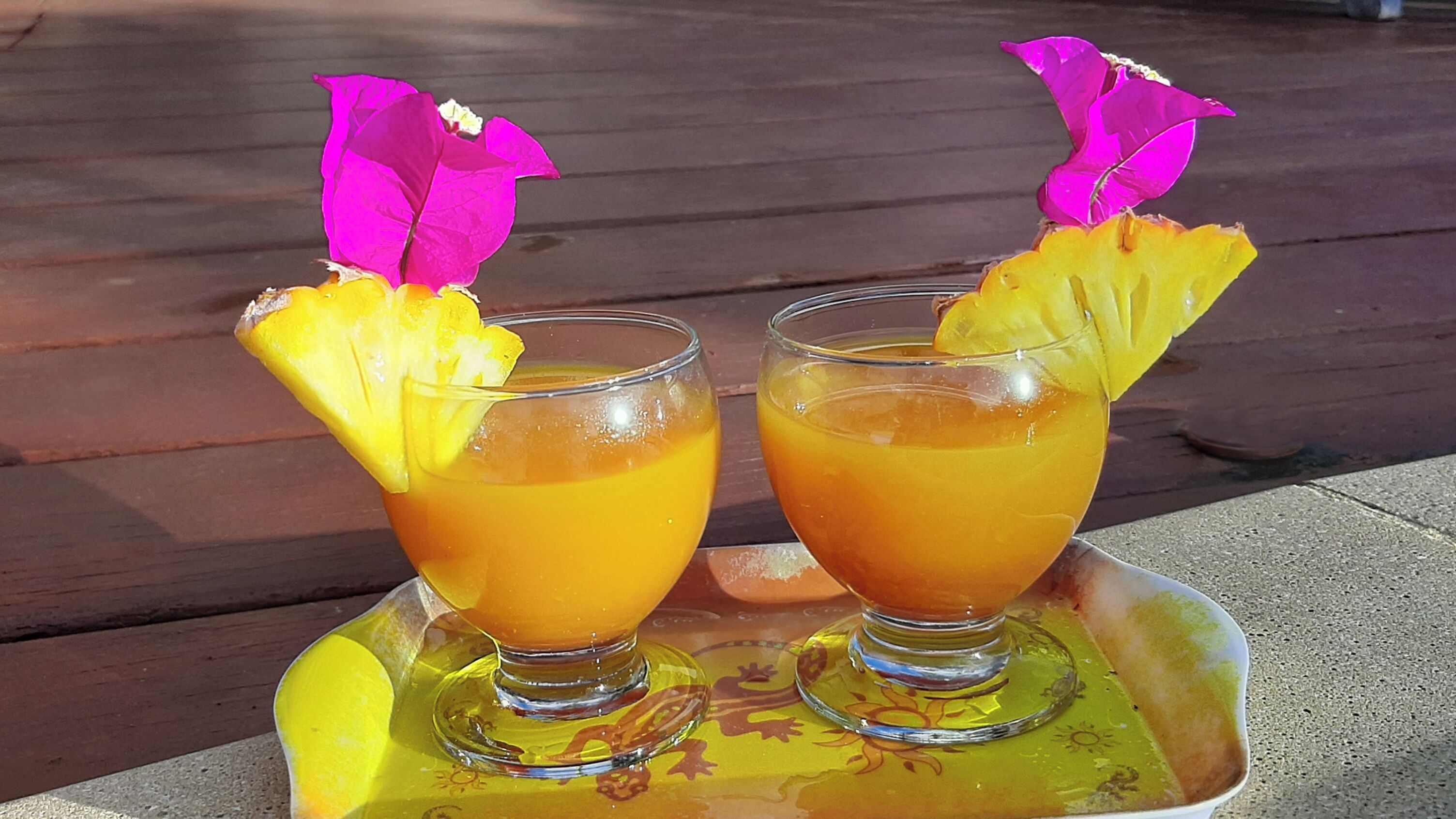 Two glasses of orange beverage with pineapple garnish on a tray.