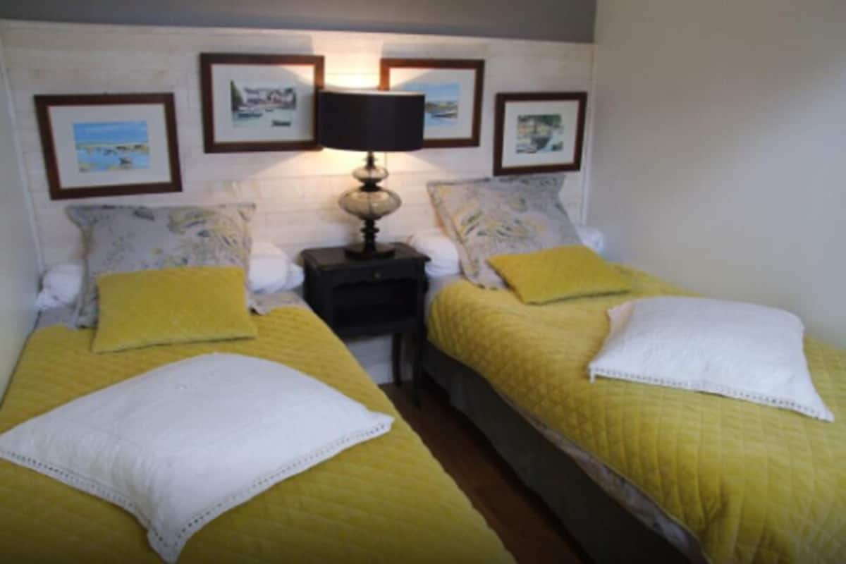 Habitación con cama doble, ropa de cama amarilla, una mesita de noche con lámpara y cuadros en la pared.