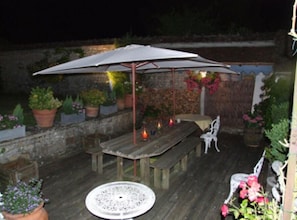 An outdoor patio with a wooden table and benches, surrounded by potted plants and a large umbrella. - Les Glycines (Ury)