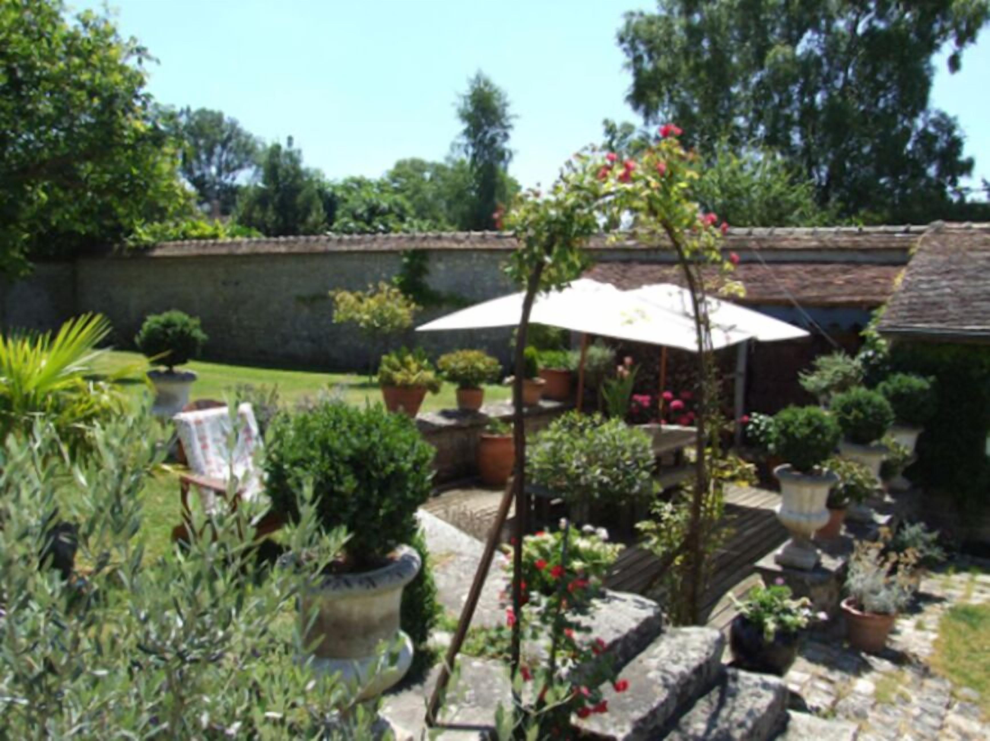 A garden with potted plants, a stone bench, and a white umbrella.