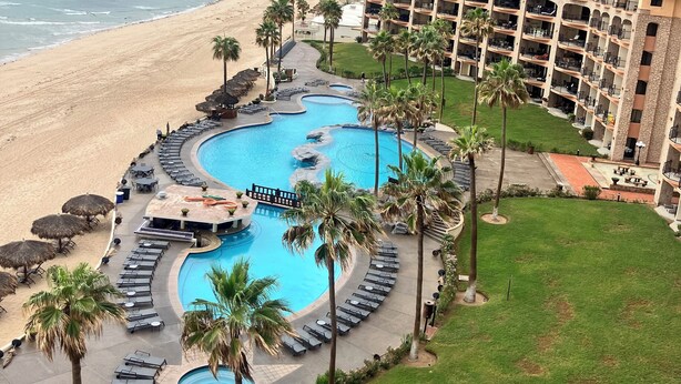 Un resort con una grande piscina, palme e vista sulla spiaggia.