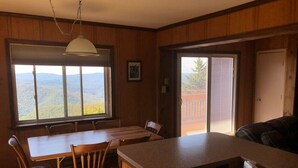 A wooden interior with a dining table, chairs, a kitchen island, a hanging light fixture, and a large window with a view of mountains. - Perfect For Large Families & Groups - Excellent Location (Snowshoe)