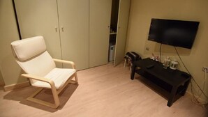 Habitació amb terra de fusta, una cadira amb coixí blanc, un suport televisió negre amb televisor de pantalla plana i un armari amb portes corredisses.