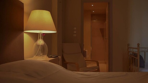 Habitació d'hotel amb llit, una làmpada de nit, una cadira i una barana de fusta.
