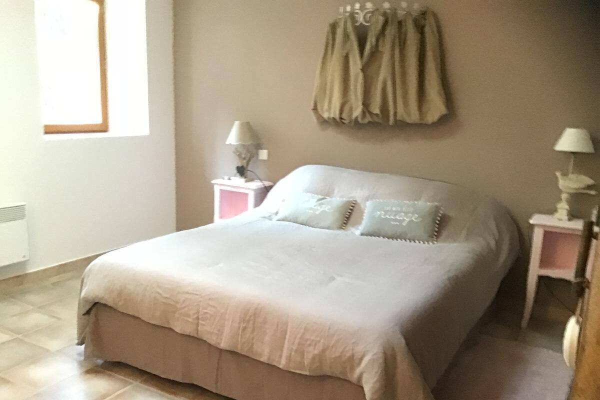 A neatly arranged bedroom with a bed, two bedside tables with lamps, a window with blinds, and a wall-mounted curtain.