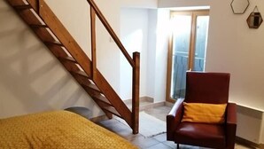 A room with a wooden staircase, a bed with a patterned blanket, a red armchair, and a painting on the wall. - Le rêve d'Emma Chambres d'hôtes (Plan-d'Orgon)