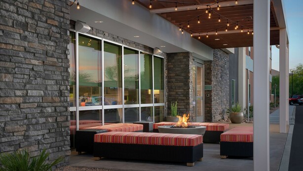 A covered outdoor seating area with stone walls, large windows, and a fire pit. - Home2 Suites by Hilton Phoenix Airport South (Phoenix)