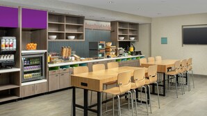A modern kitchen area with a dining table and chairs, equipped with a refrigerator, microwave, and various food items. - Home2 Suites by Hilton Phoenix Airport South (Phoenix)