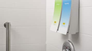 A bathroom with a white tiled wall, a chrome shower control panel, and two soap dispensers labeled "Neutrogena Invigorating" and "Neutrogena Shower Gel".