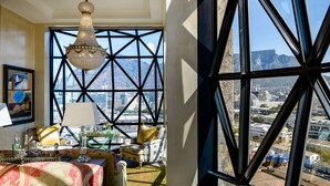 A room with a large window, a chandelier, a table with a tablecloth, and a chair with a cushion. - The Silo Hotel (Cape Town)