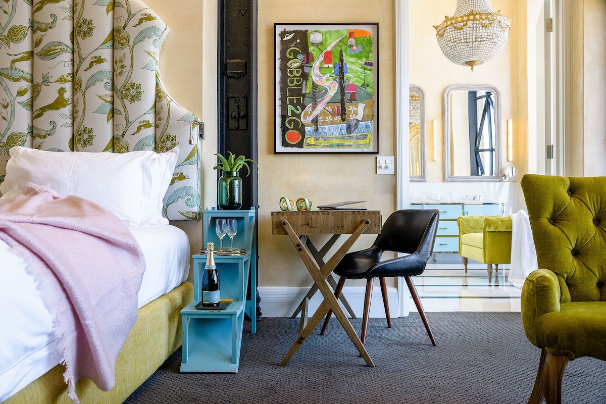 A bedroom with a bed, a desk, a chair, and a green armchair.