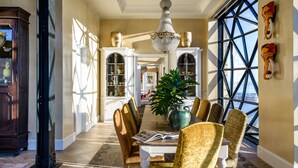 A dining area with a chandelier, wooden chairs, a table with a book, and a large window with a view. - The Silo Hotel (Cape Town)