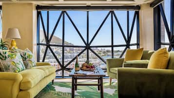 Una habitación con un sofá amarillo, un sillón verde y una mesa de centro con una botella y fruta.