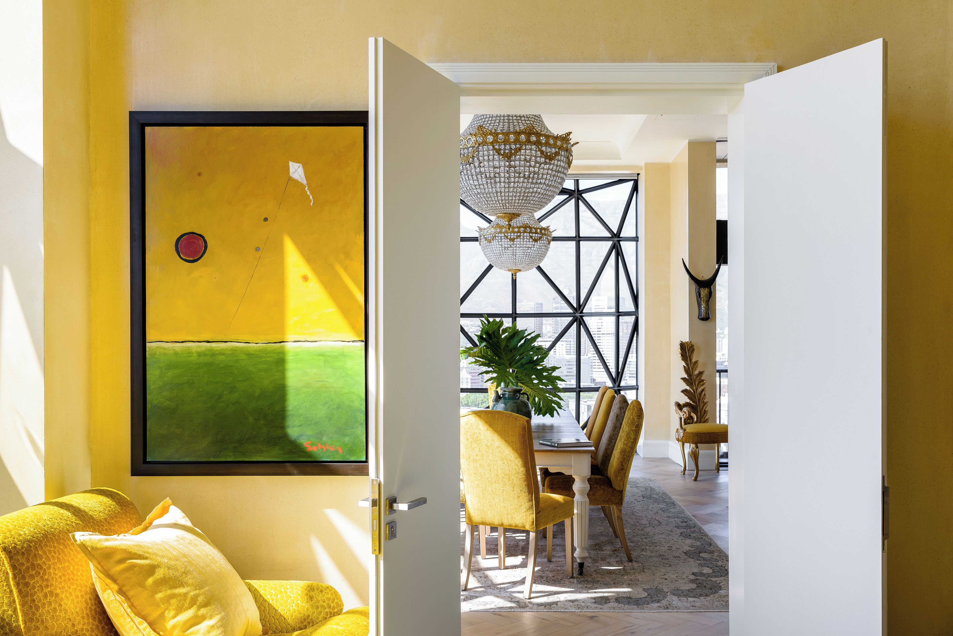An interior with a dining area, a yellow sofa, and a large window with a geometric pattern.