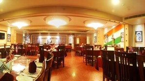 Un comedor amplio con varias mesas y sillas, una araña central y cuadros en las paredes.