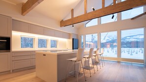 Eine moderne Küche mit einer zentralen Kochinsel, Barhocker und großen Fenstern mit Blick auf eine verschneite Landschaft.
