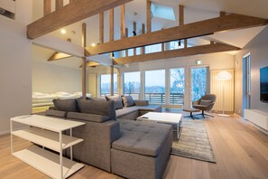 A modern living room with a sectional sofa, a white coffee table, and a floor lamp. There is a large window providing a view of the outdoors. - Yoteiyama House (Kutchan)