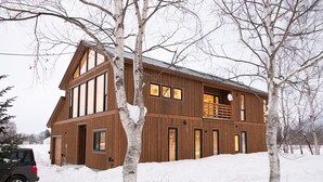 Ein großes, mehrstöckiges Holzhaus mit Balkon, umgeben von verschneitem Gelände und kahlen Bäumen.