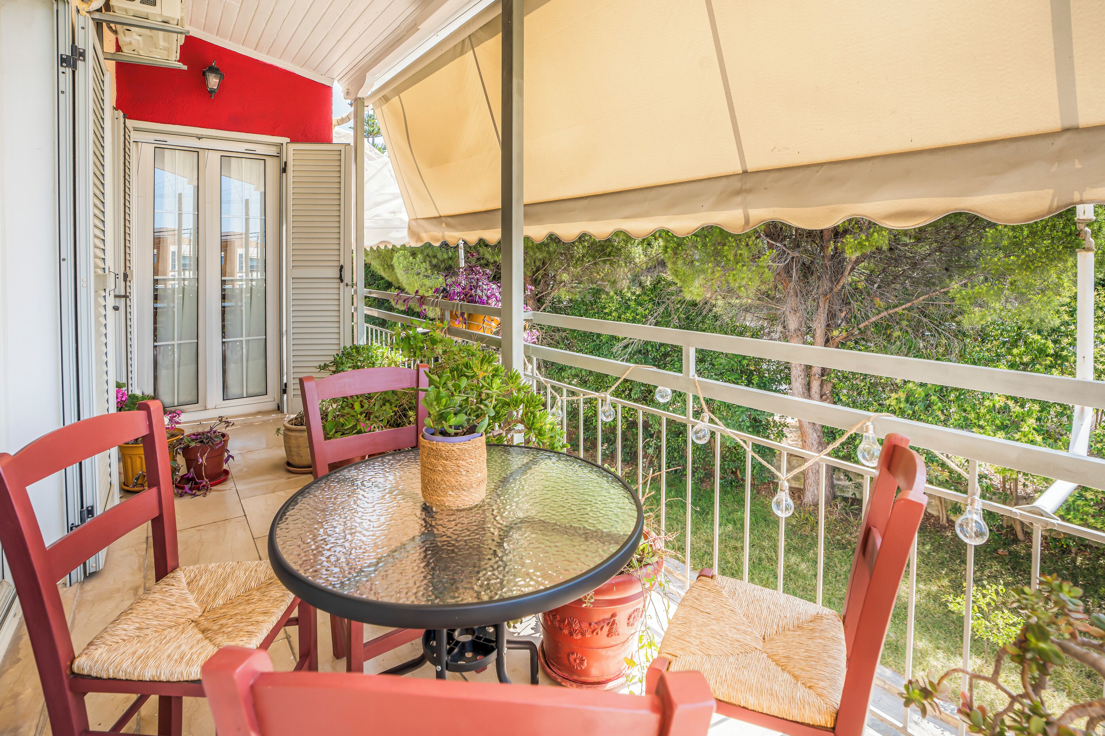 Un balcon avec une table en verre, des chaises rouges et des plantes en pot.