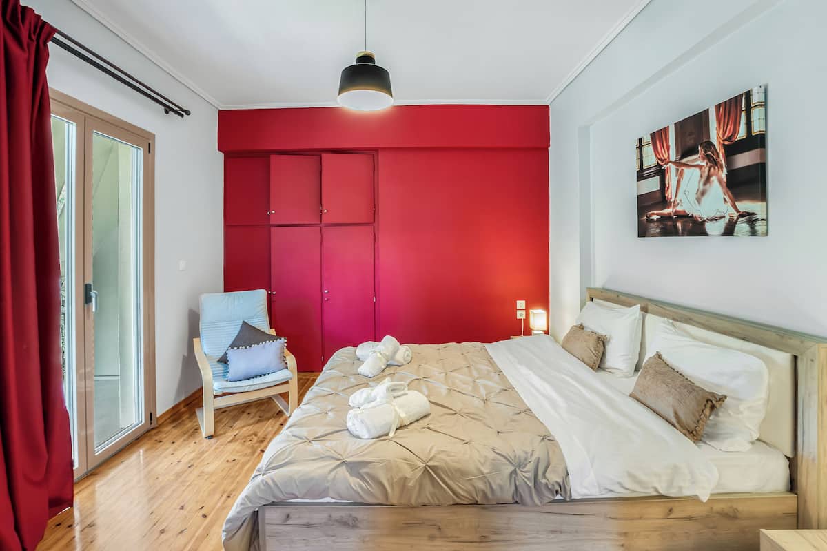 Ein Schlafzimmer mit roter Wand, einem Bett mit weißer Bettwäsche, einem Sessel mit Kissen und einem Gemälde an der Wand.