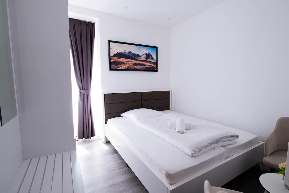 A modern hotel room with a large bed, a headboard, a painting on the wall, and a window with curtains.