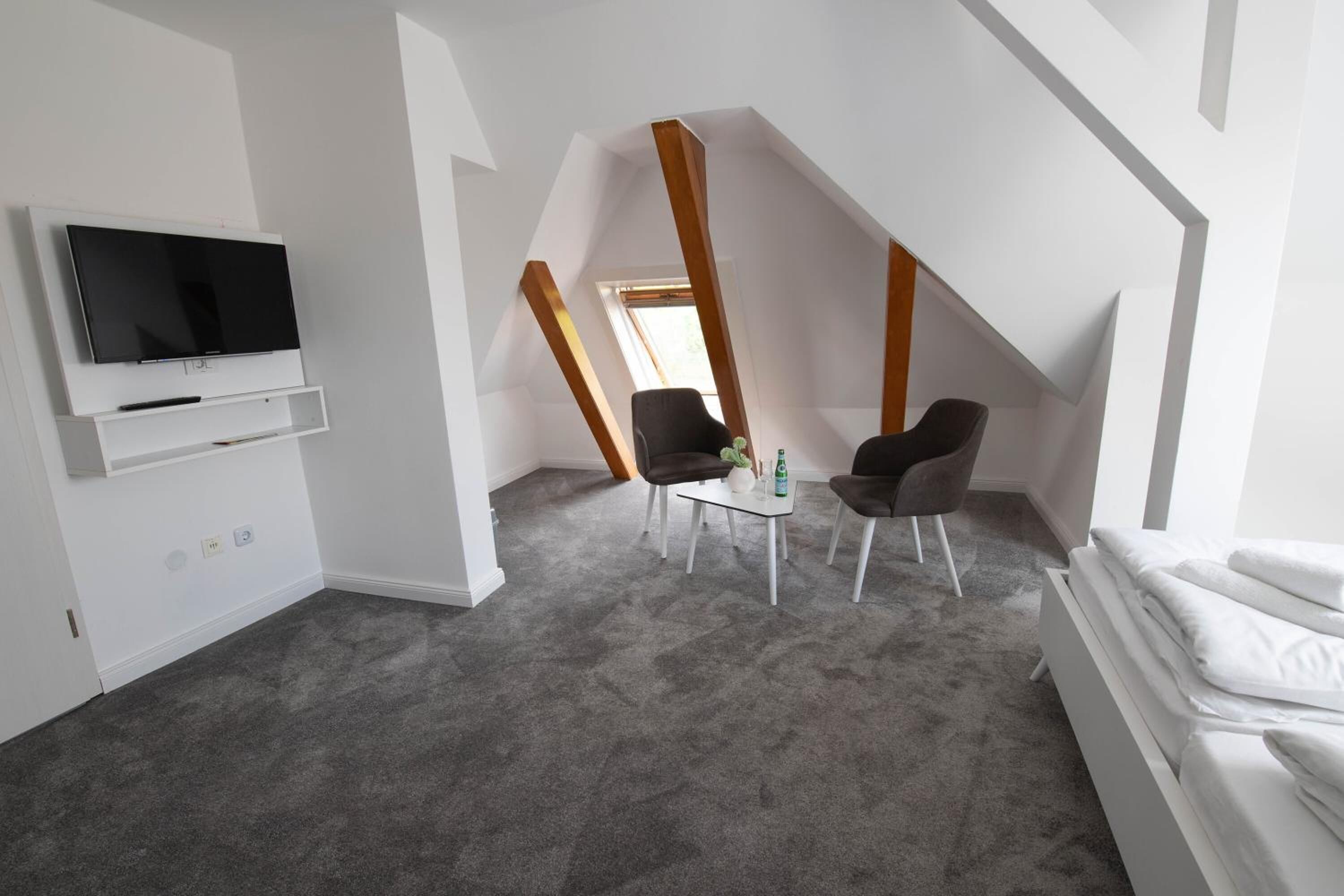 Una habitación moderna con televisión, dos sillones, una mesita y una cama.