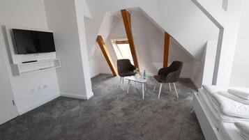 Una habitación moderna con televisión, dos sillones, una mesita y una cama.