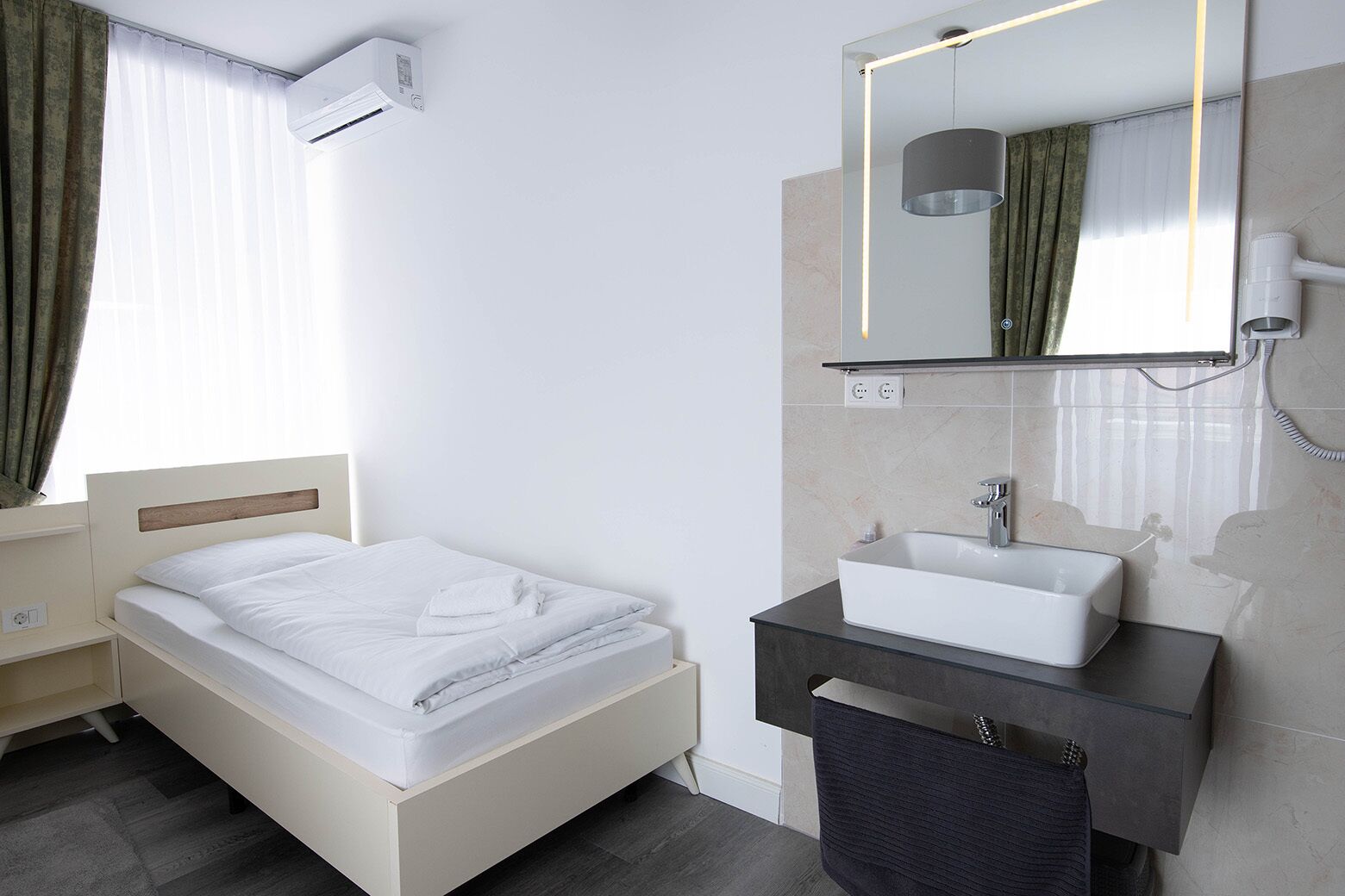 Une chambre d’hôtel moderne équipée d’un lit, d’une coiffeuse avec miroir et d’un appareil de climatisation.
