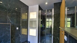 A modern bathroom with dark marble walls, a glass shower enclosure, and a wooden vanity. - Heidepension (Bispingen)