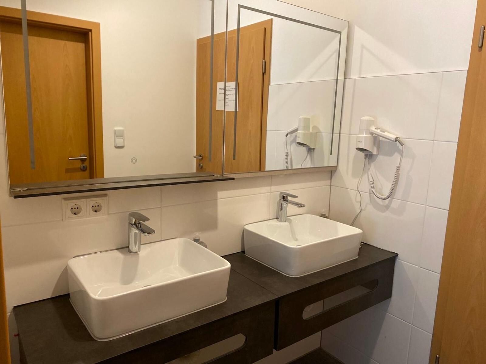 Un baño con dos lavamanos, un espejo y un secador de pelo.