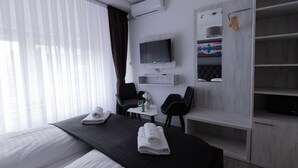 A hotel room with a bed, a desk, a chair, a TV, and a wardrobe.
