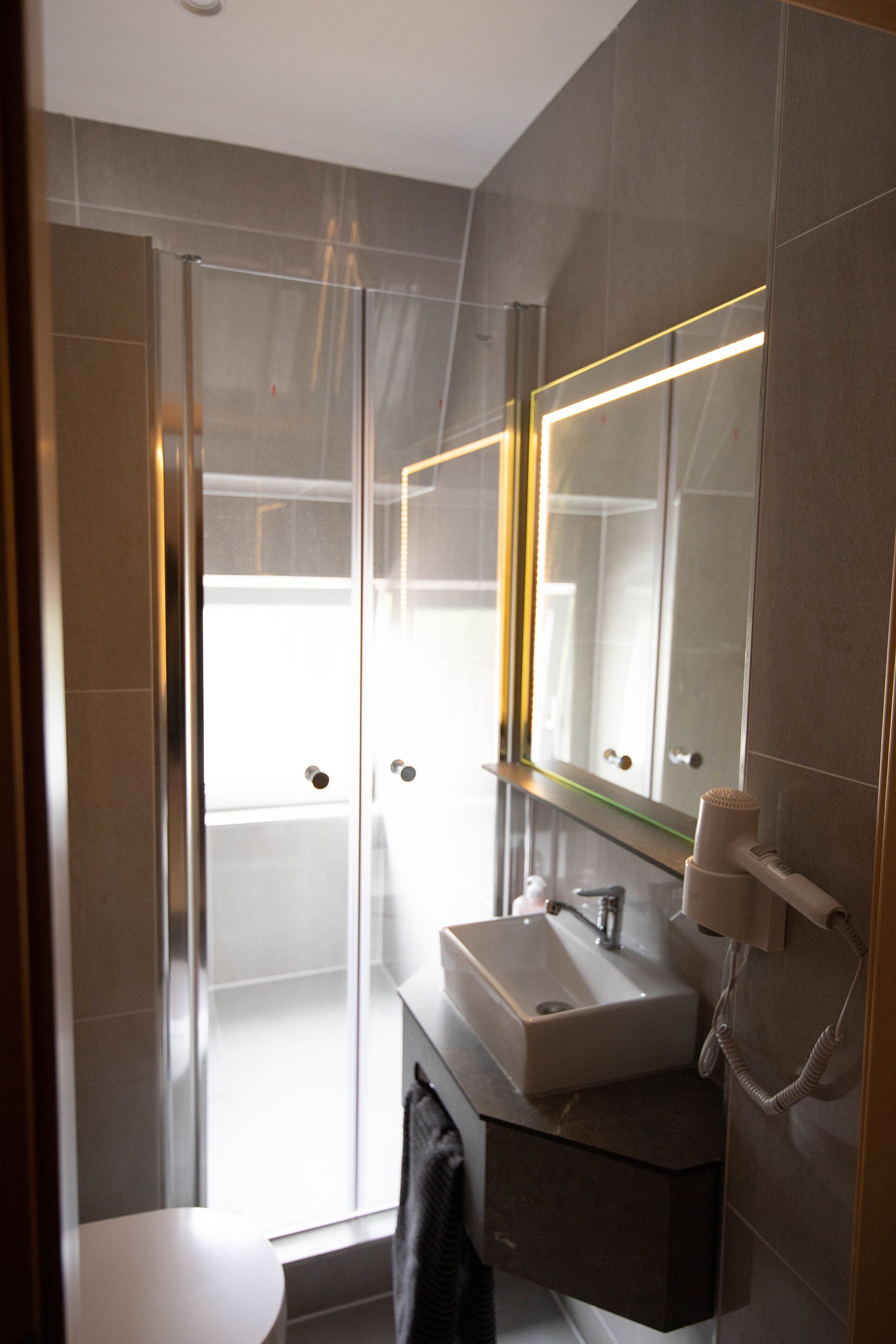 Un baño moderno con cabina de ducha de vidrio, un lavabo con espejo y un perchero para toallas.