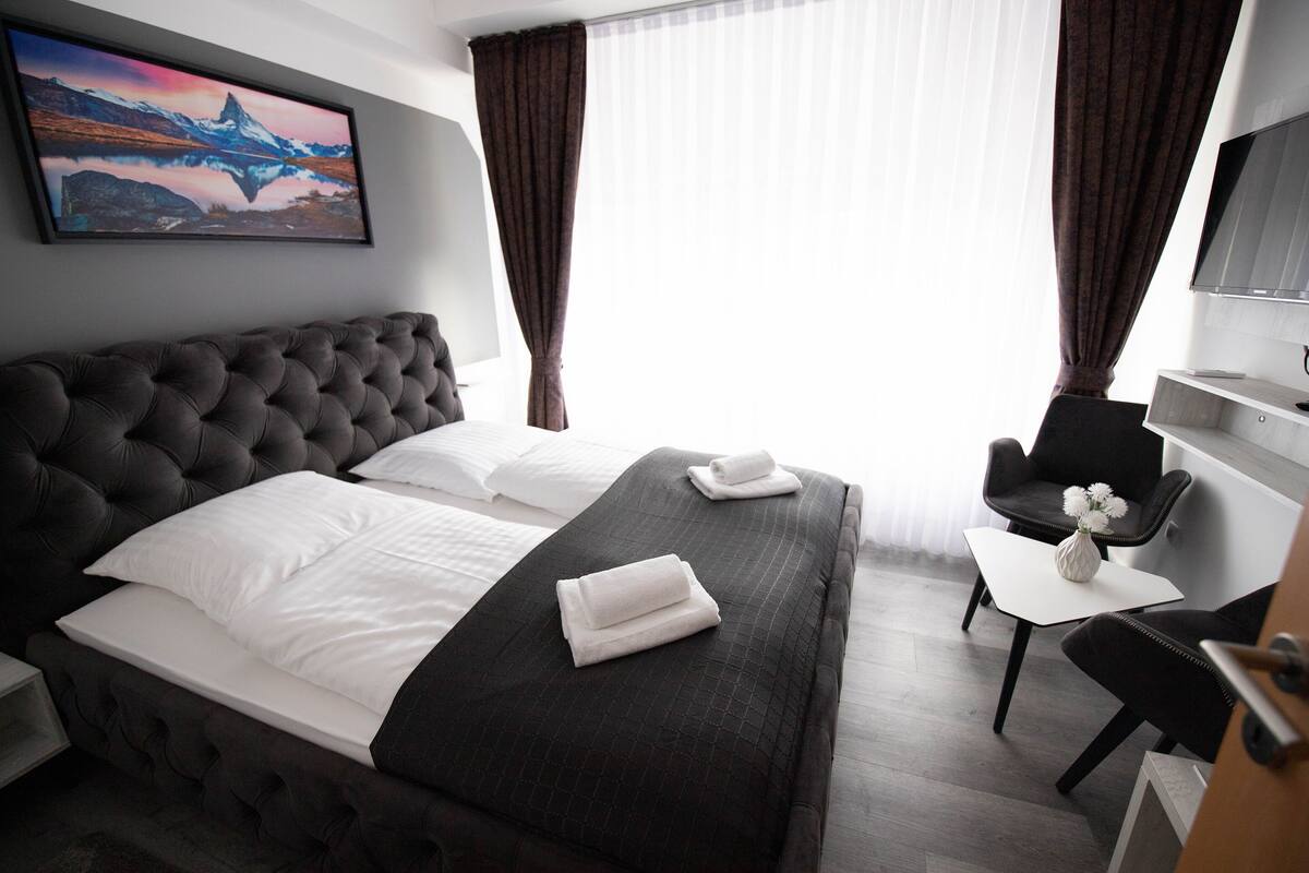 A hotel room with a large bed, a small desk, a chair, and a TV.