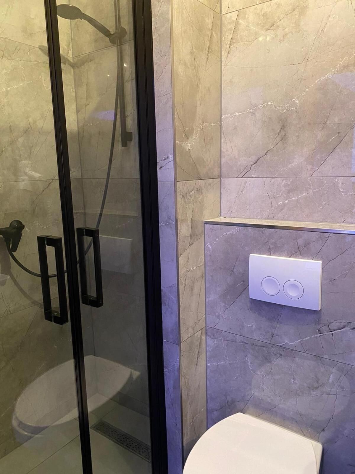 Ein modernes Badezimmer mit einer gläsernen Duschkabine, einer Toilette und einer an der Wand befestigten Bedienanlage.