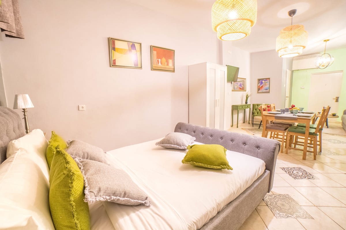 A bedroom with a bed, pillows, a lamp, and a dining area with chairs and a table.